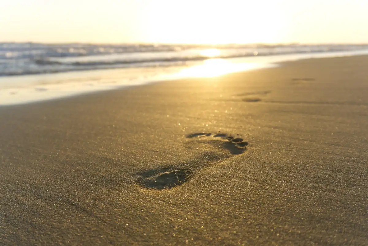 Footprints in the sand on a Maui beach at sunset, with a vibrant sky.