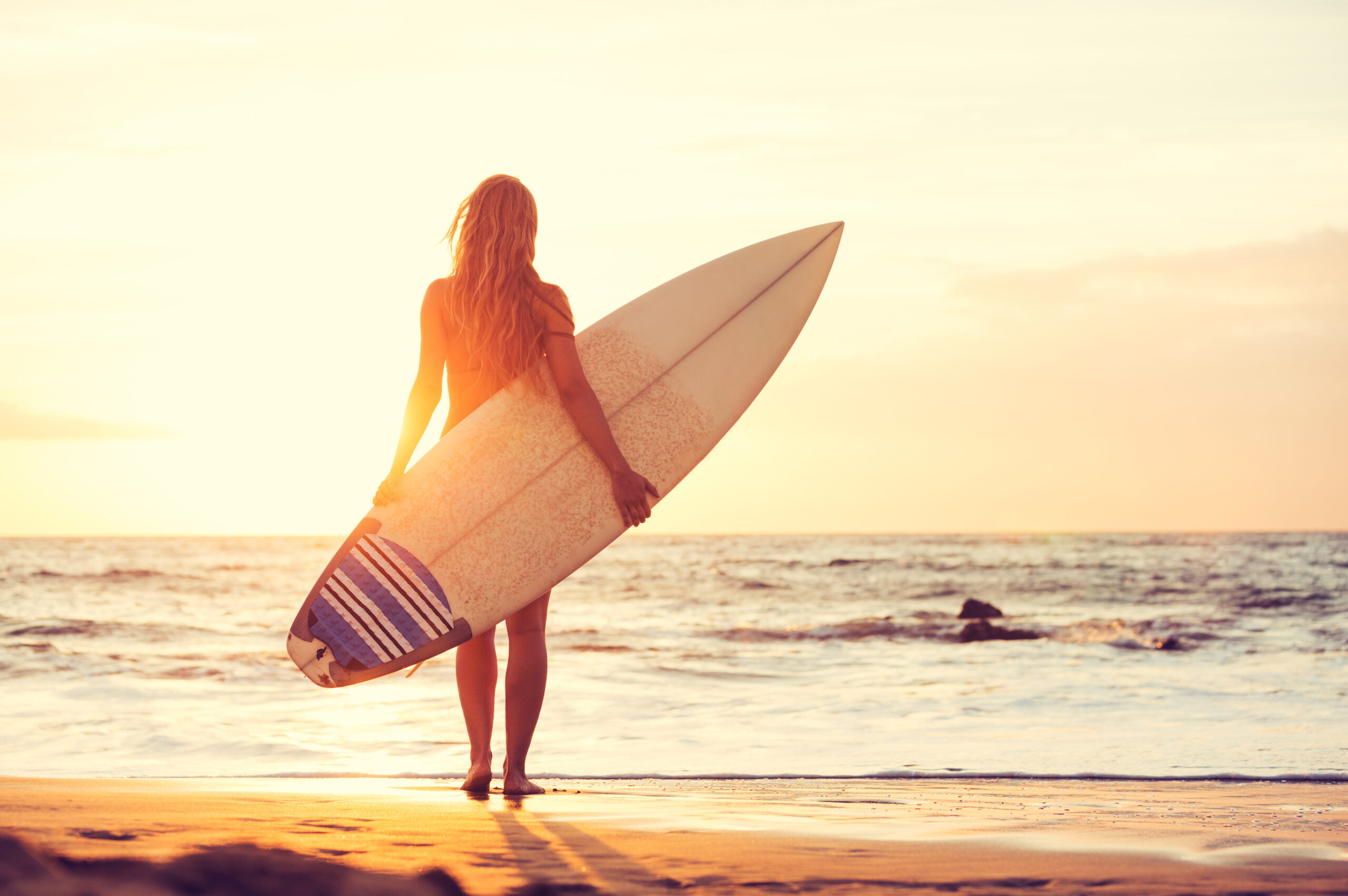Woman with a surfboard on a beach at sunset on Maui.