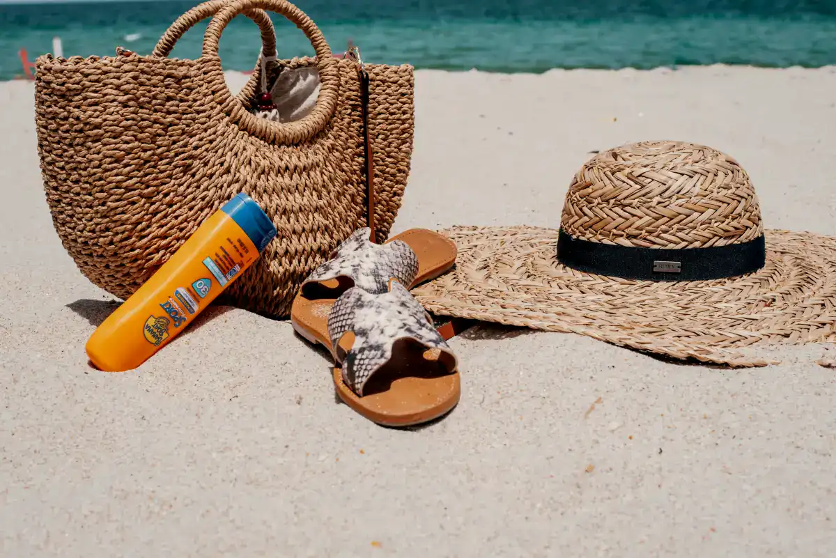 Sandal, sunscreen, bag, hat on a sandy beach in Maui.