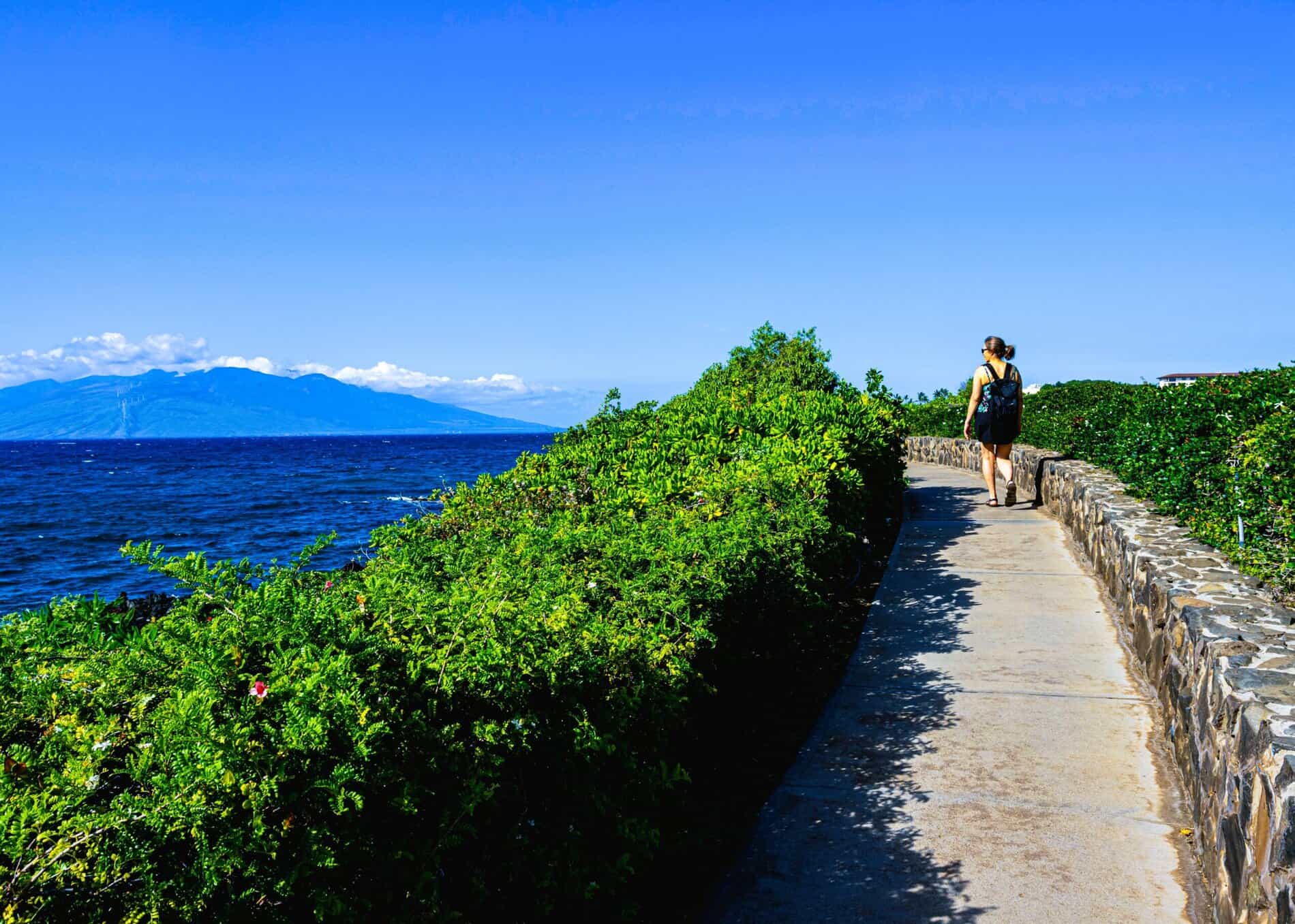 Woman walking at Wailea broad walk with breathtaking ocean and mountain backdrop on Maui.