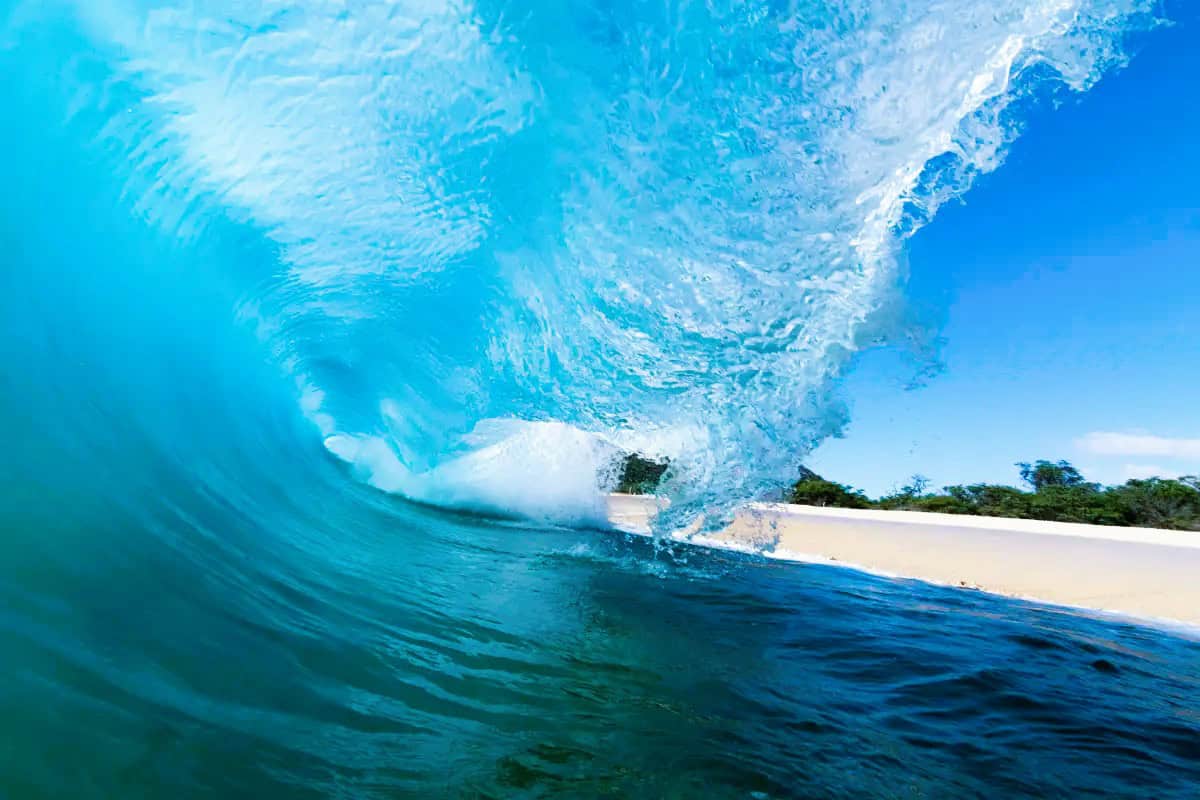A dramatic wave breaking on a Maui beach, with white foam contrasting against the blue water.