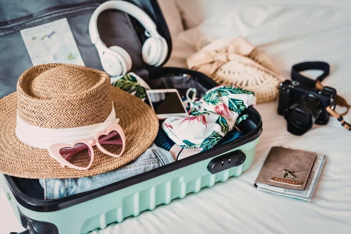 A suitcase with sunglasses and a hat on a bed, ready for a trip to Big Island, Hawaii.