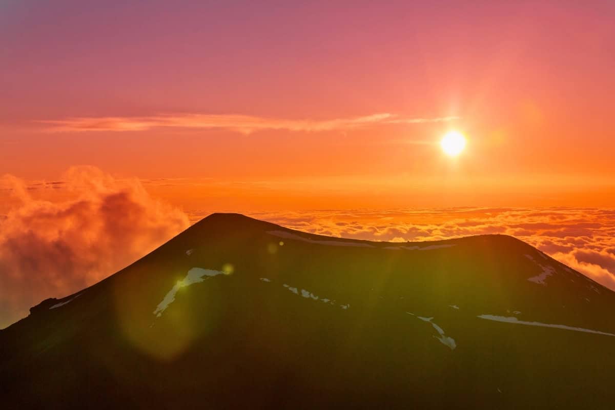 A breathtaking sunset at Mauna Kea summit, with vibrant colors spilling over the mountain's silhouette.